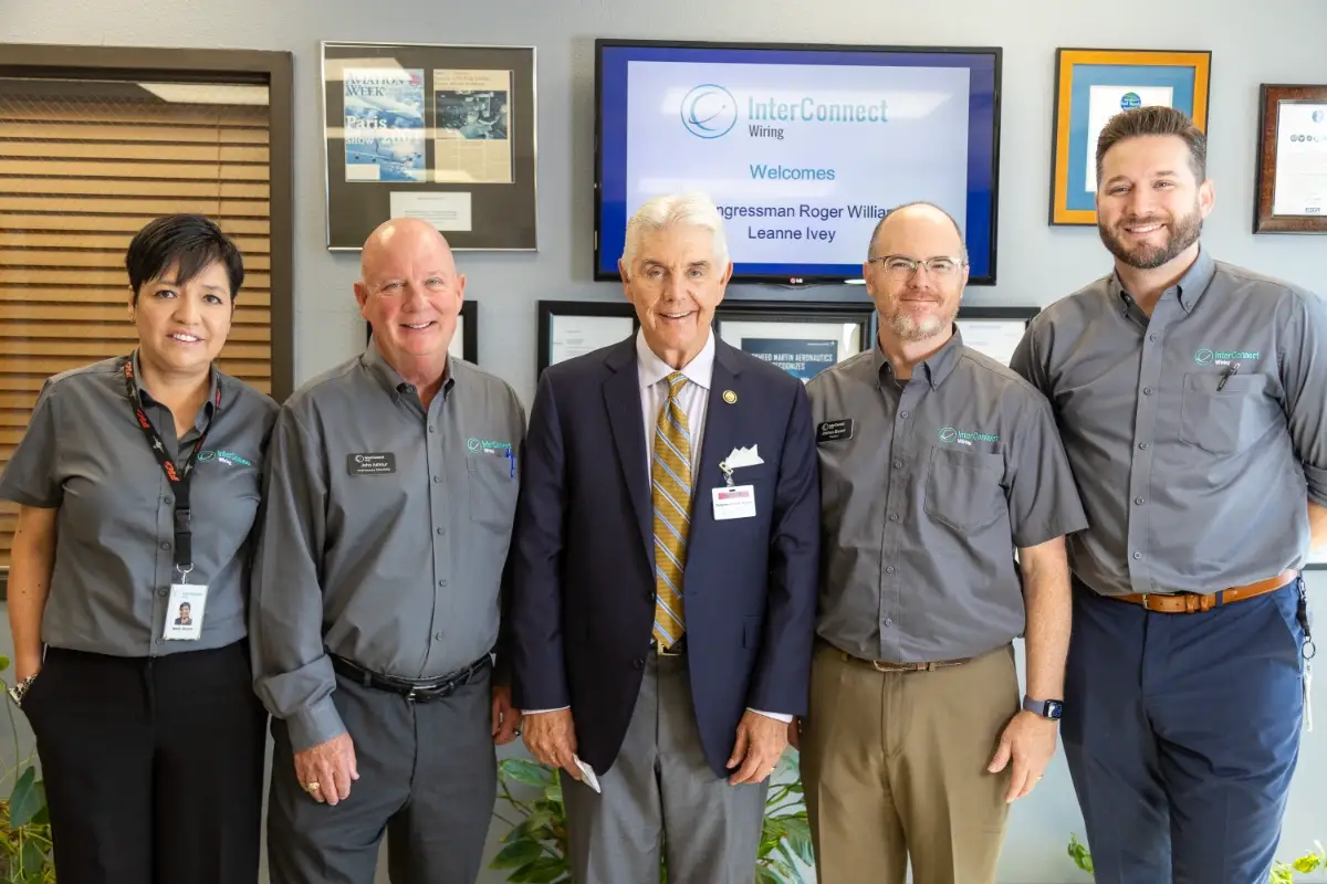 Group of five, four in InterConnect Wiring shirts, posing in front of a screen welcoming Congressman Roger Williams.