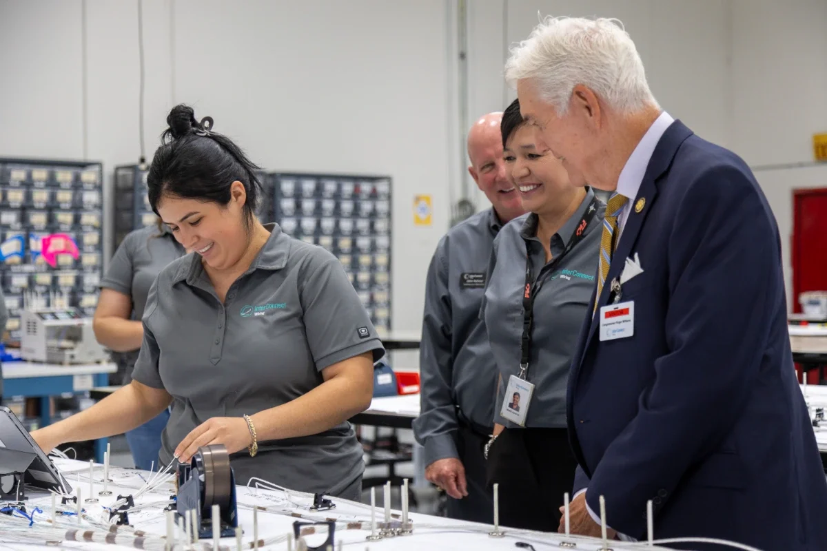 An InterConnect Wiring employee builds a wire harness while Congressman Roger Williams and two colleagues look on.